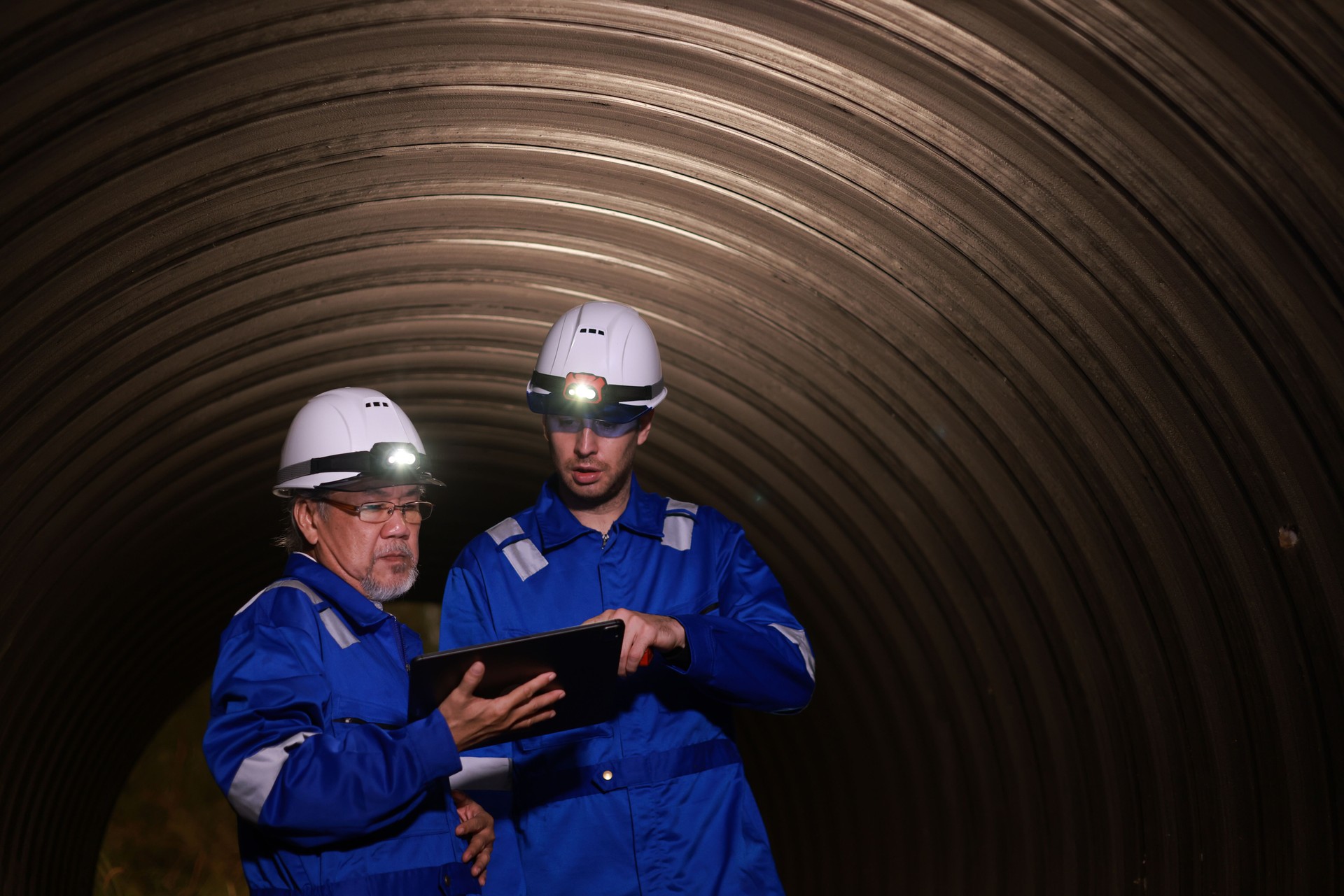 Ingenieros superiores e ingenieros de obra con uniformes de seguridad con faros que trabajan en túneles de construcción o en enormes tuberías de aguas residuales
